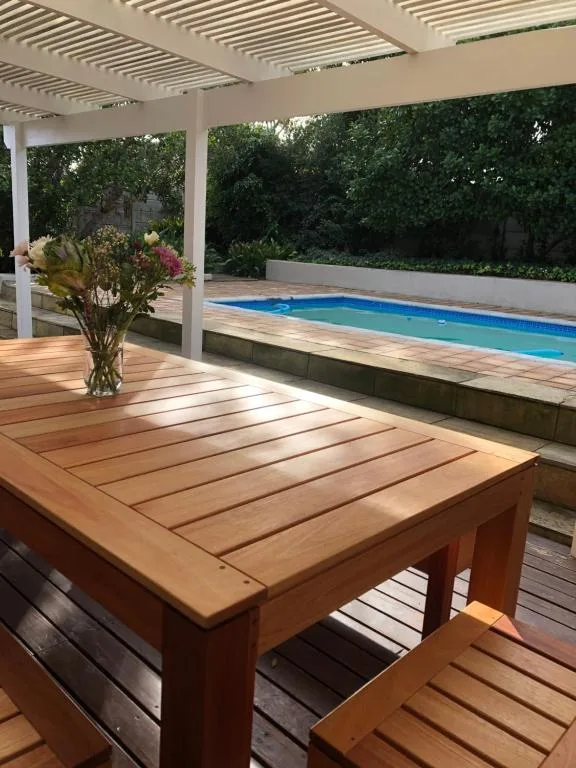 Wooden deck with dining table overlooking heated swimming pool and pergola