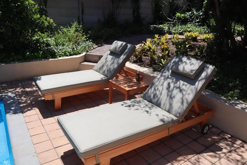 Wooden sun loungers with cushions on tiled patio surrounded by lush garden