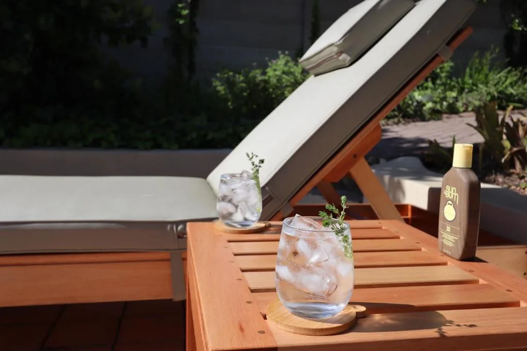 Wooden deck with refreshing cocktails and sunscreen bottle overlooking garden
