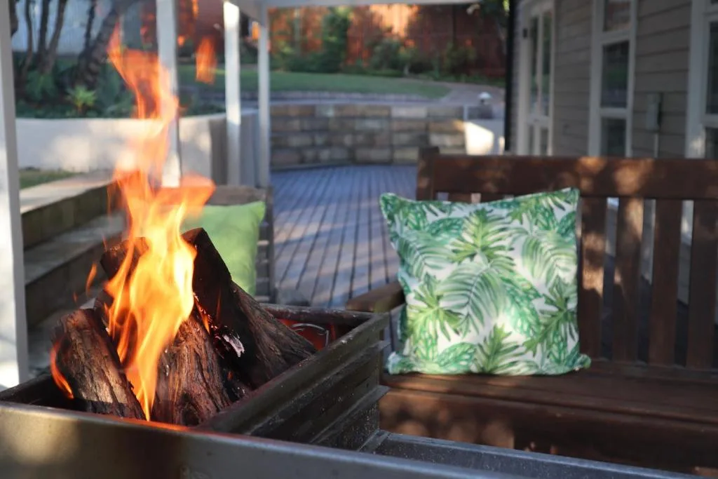 Outdoor fire pit with flames on spacious wooden deck overlooking garden