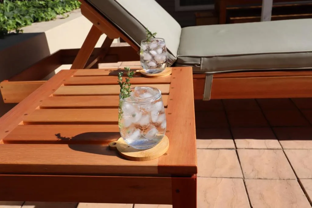 Wooden outdoor table with refreshing drinks and rosemary garnish on sunny patio