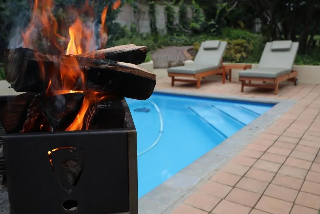 Firepit burning brightly beside heated pool with loungers and garden views