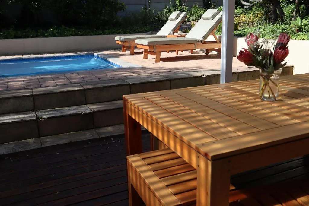 Wooden deck with dining table overlooking heated swimming pool and loungers