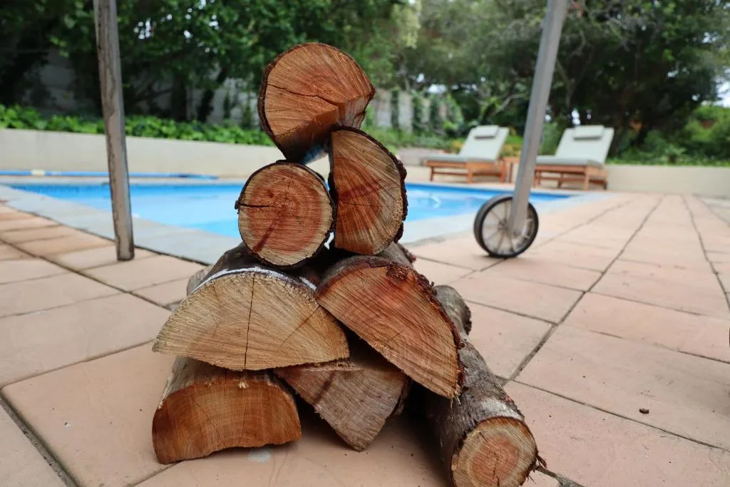 Stacked firewood logs poolside with swimming pool and loungers in background