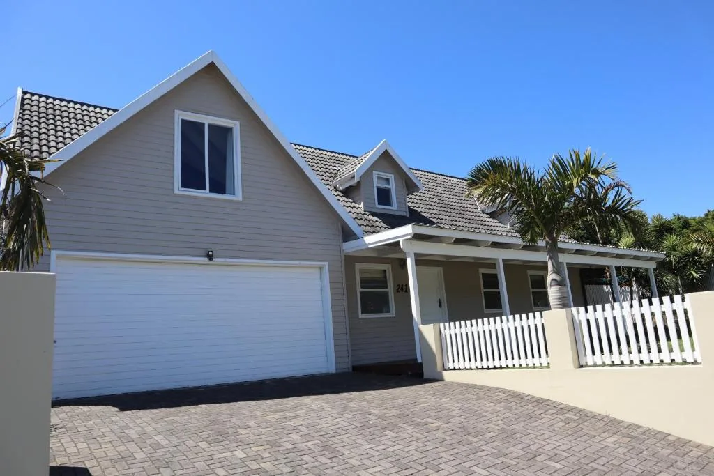 Modern white house with garage, white fence, and palm trees on driveway
