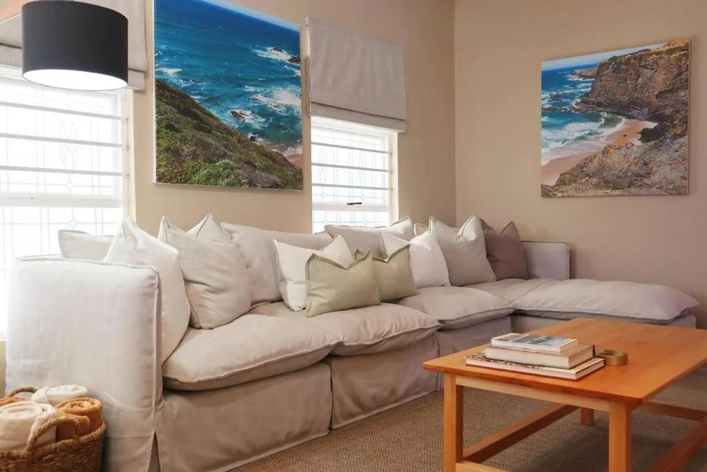 Bright living room with cream sofa, coastal artwork, wooden table, and natural light