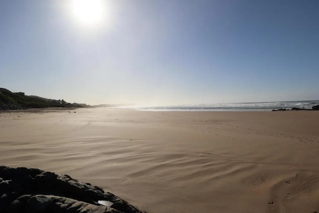 Expansive sandy beach with gentle waves and rocky shoreline on sunny day