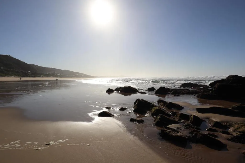 Scenic beach with rocky outcrops, golden sand, and distant coastal hills