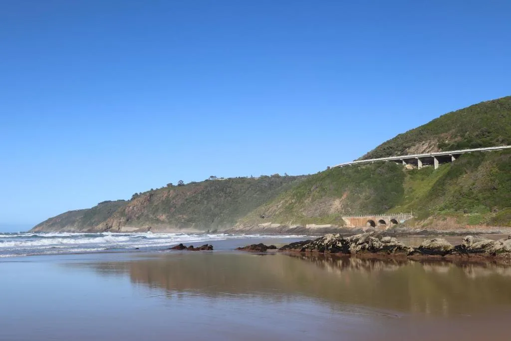 Scenic coastal beach with green cliffs and bridges in distance