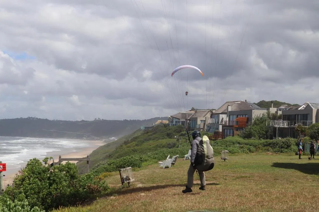 Coastal cliffside properties overlooking beach with paraglider above