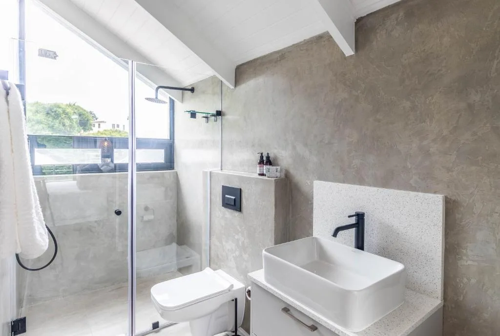 Modern bathroom with glass shower enclosure, white vessel sink, and concrete accent wall