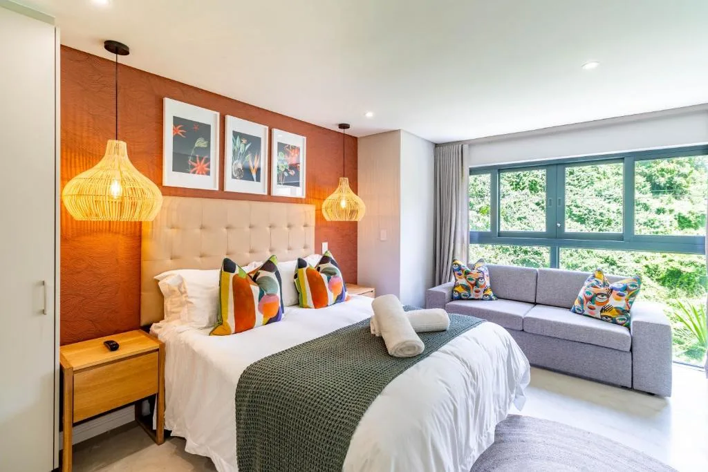 Spacious bedroom with queen bed, colorful pillows, pendant lights, and lounge seating