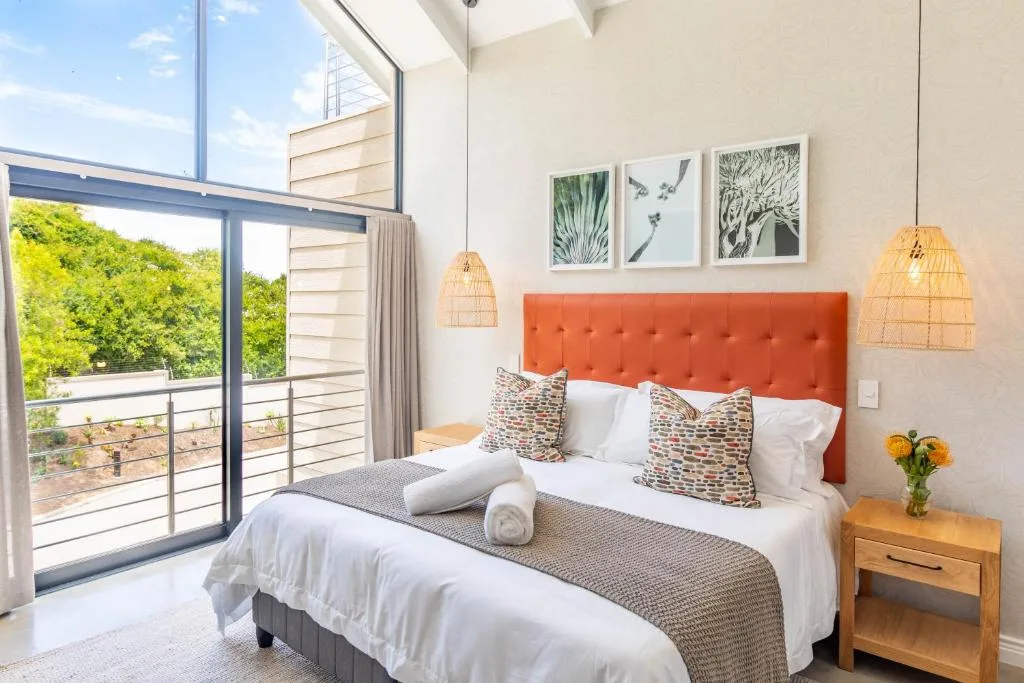 Modern bedroom with orange headboard, white bedding, and balcony overlooking lush gardens