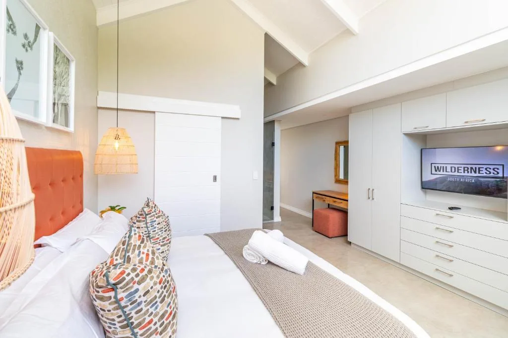 Bright modern bedroom with orange headboard, pendant lighting, and TV entertainment area