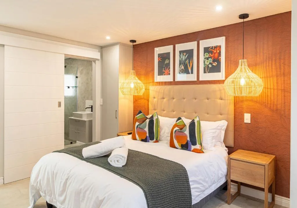 Modern bedroom with queen bed, orange accent wall, pendant lights, and en-suite bathroom