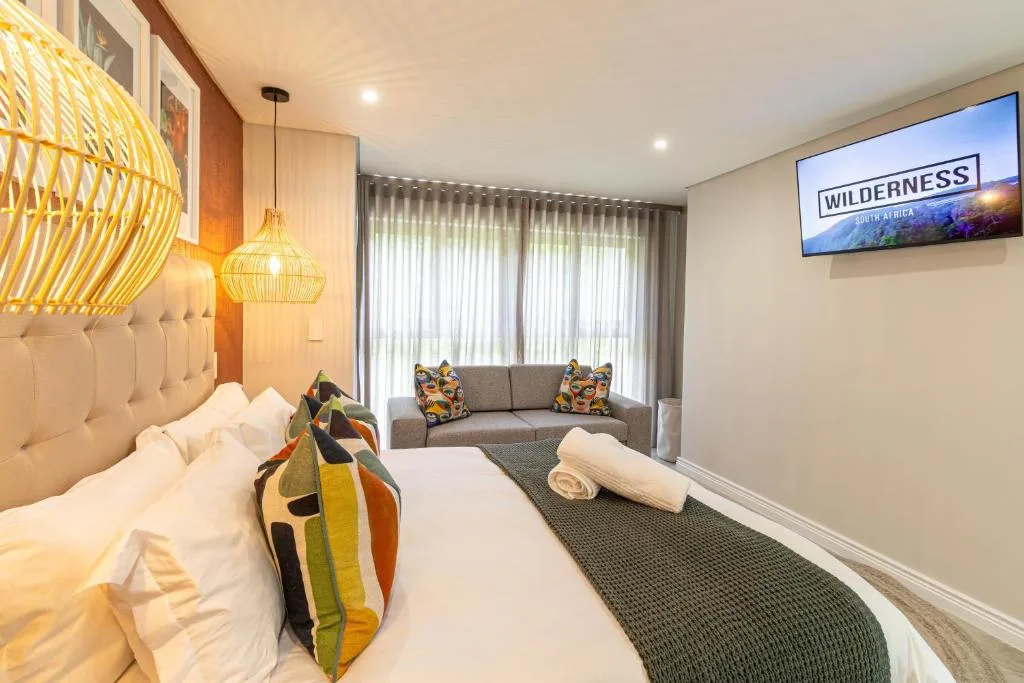 Modern bedroom with bed, lounge area, and large windows overlooking garden