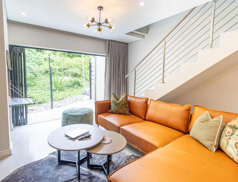 Modern living room with orange leather sofa, pendant lighting, and garden access