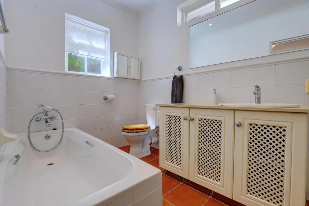 Bright bathroom with white bathtub, wooden vanity, and terracotta floor tiles