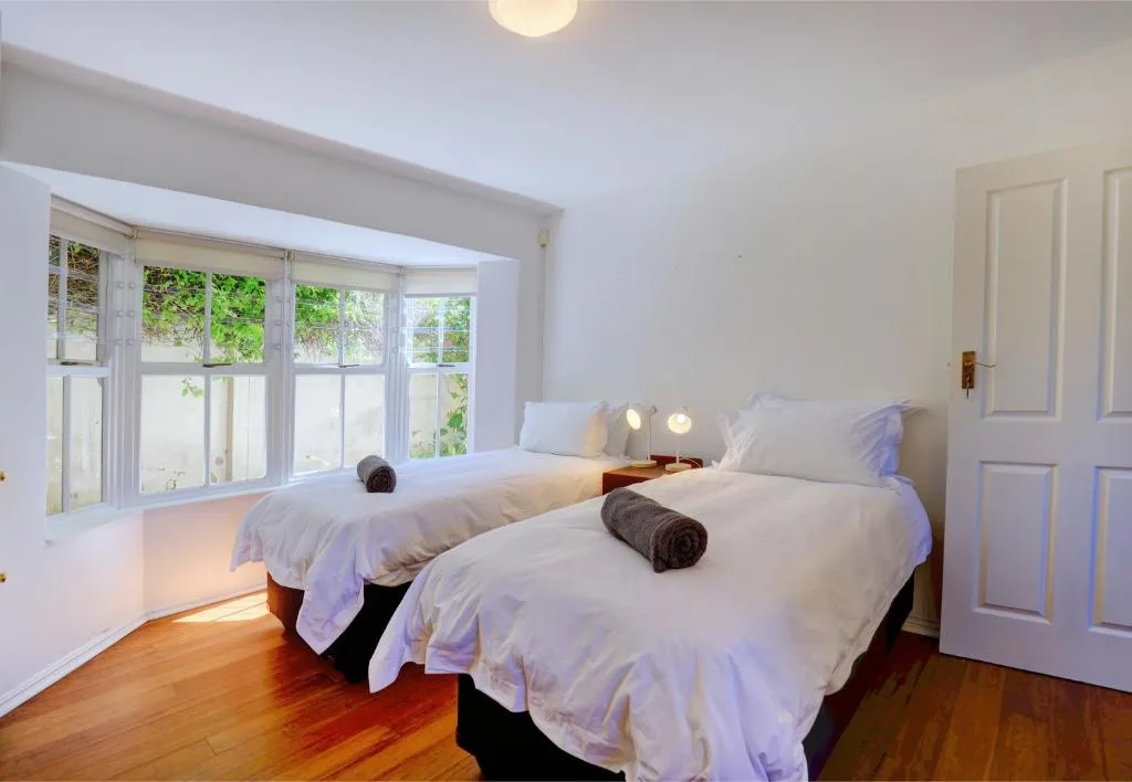 Bright bedroom with twin beds, large windows overlooking garden, wooden floors