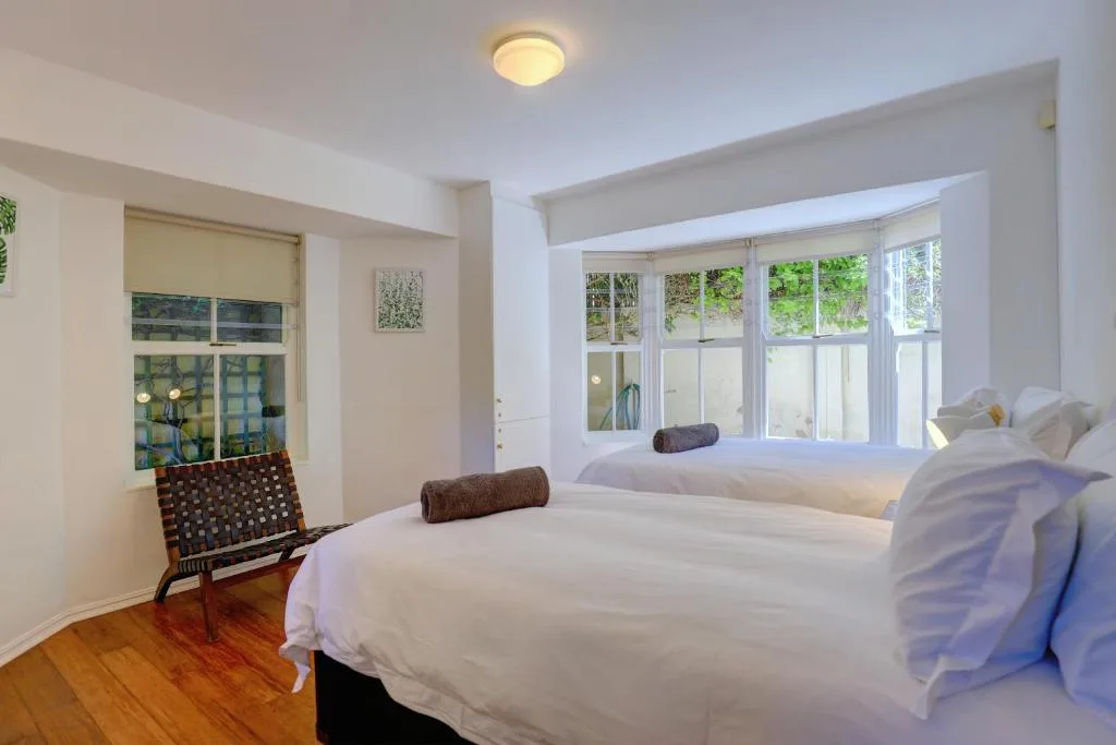 Bright bedroom with two beds, wooden floors, and large windows with garden views