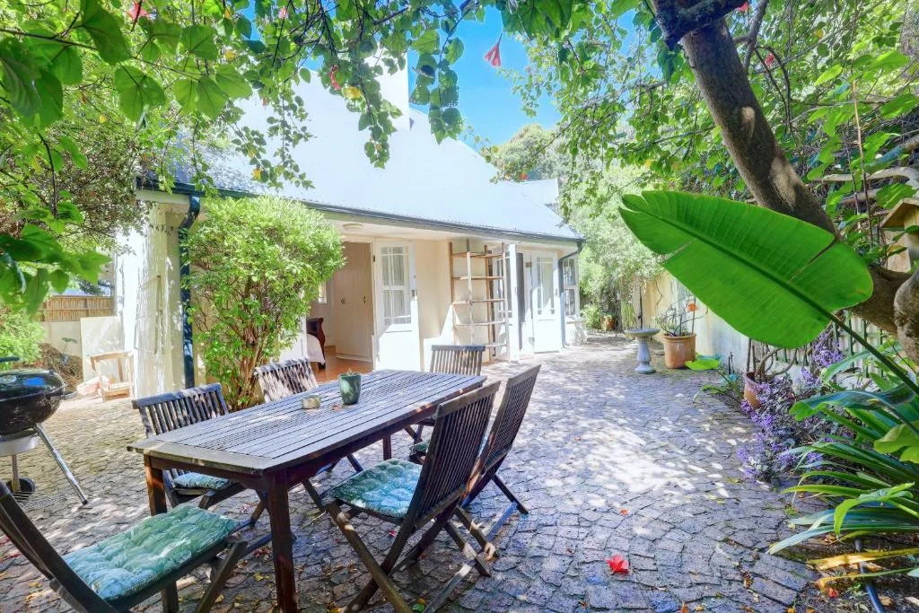 Shaded patio with dining table, chairs, and lush garden surroundings