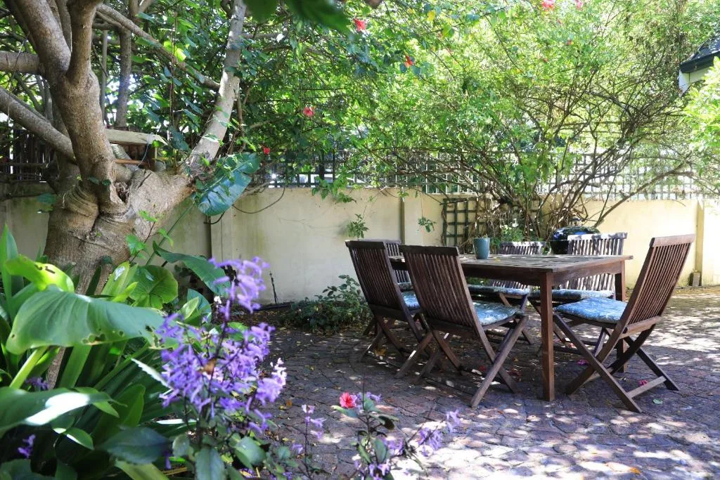 Shaded outdoor dining area with wooden table and chairs under mature trees