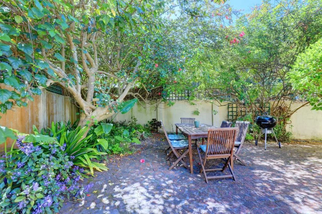 Shaded garden patio with dining table, chairs, and lush flowering plants