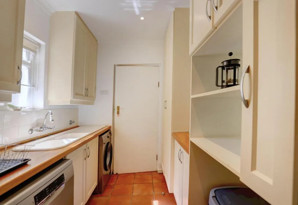 Bright galley kitchen with cream cabinetry, wooden counters, and tiled floor