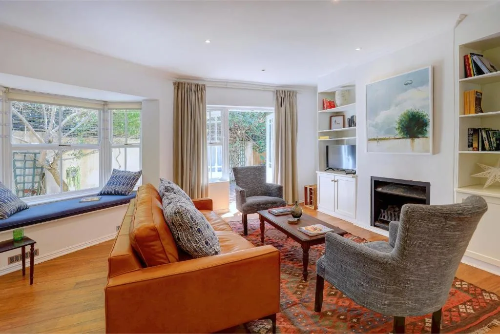 Bright living room with orange sofa, gray chairs, fireplace, and garden views