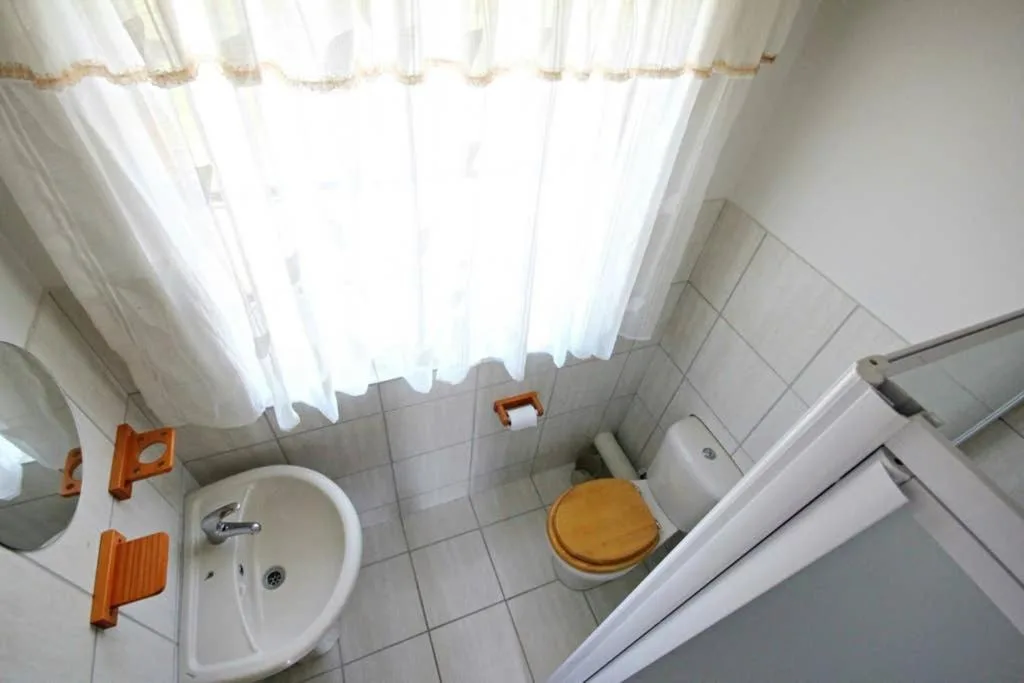 Bright bathroom with white tile floor, round sink, and wooden toilet seat