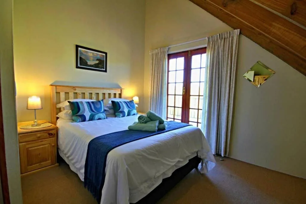 Bright bedroom with queen bed, blue striped pillows, wooden bedside table, and French doors opening to view