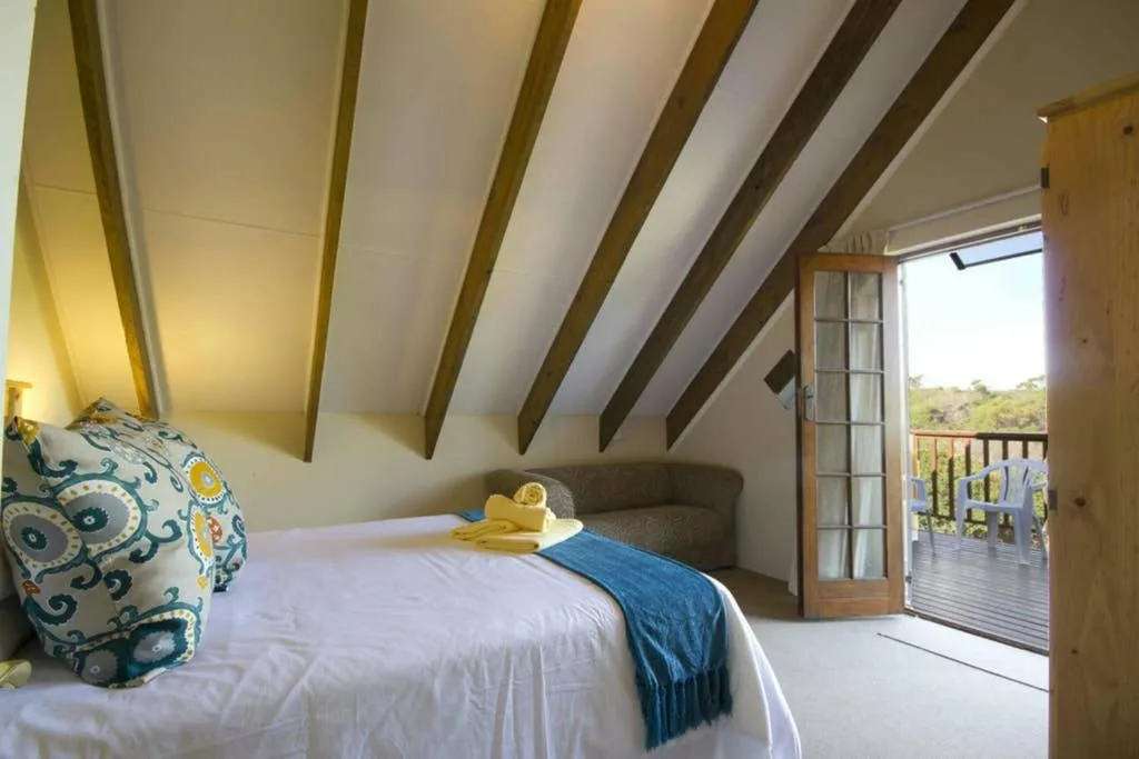 Bright attic bedroom with exposed beams and deck access overlooking garden