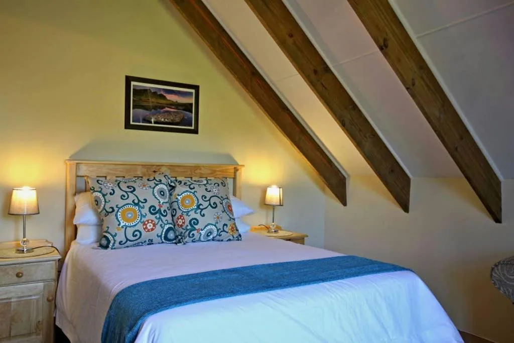 Cozy attic bedroom with wooden beams, queen bed, and warm lighting