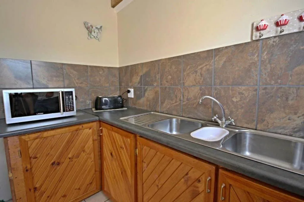 Kitchen with wooden cabinets, gray countertop, stainless steel sink, and microwave