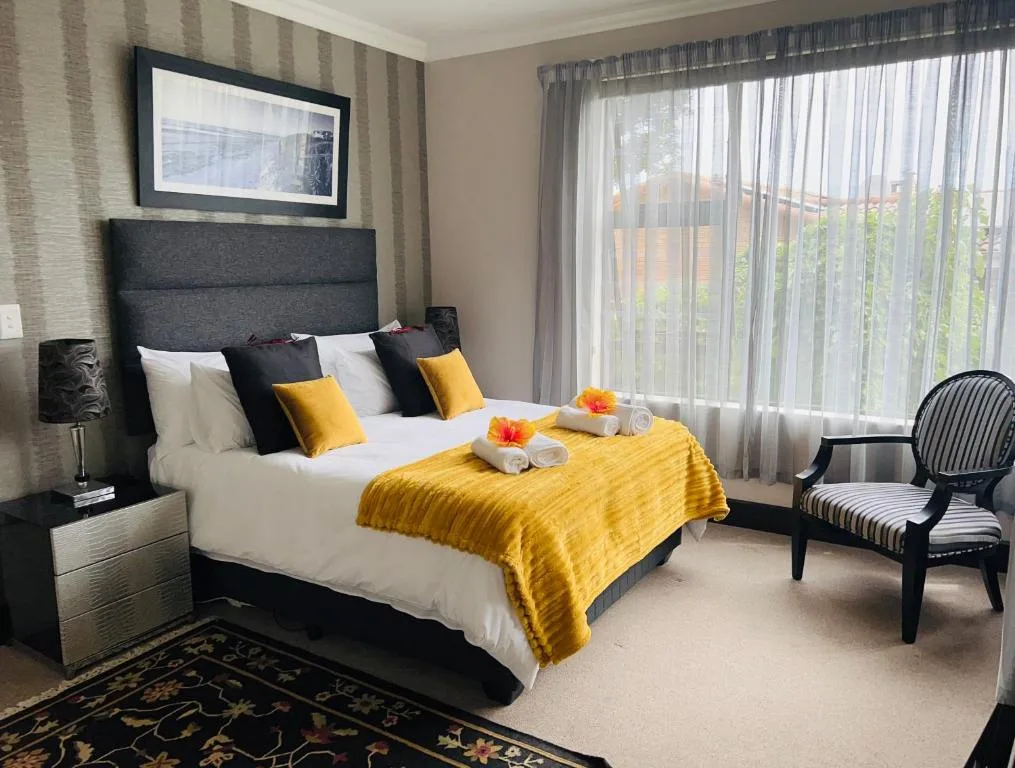 Modern bedroom with queen bed, yellow throw, and large windows overlooking garden