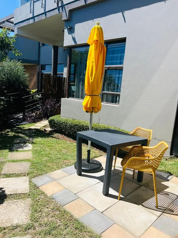 Outdoor patio with black table, yellow chairs, and bright umbrella