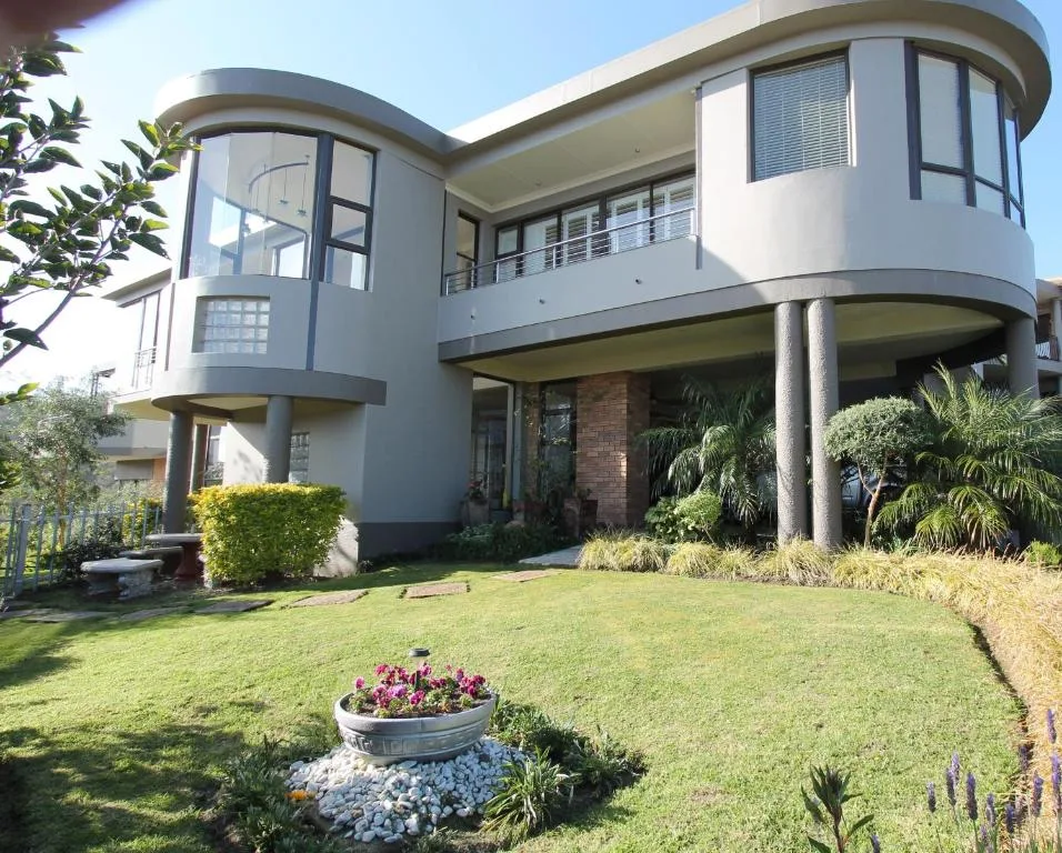 Modern curved white facade with manicured gardens and flowering beds