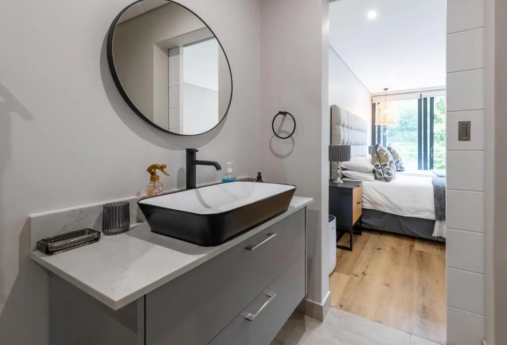 Modern bathroom with black vessel sink, round mirror, and wooden flooring