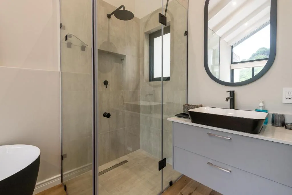 Modern bathroom with glass shower enclosure, black vessel sink, and round mirror