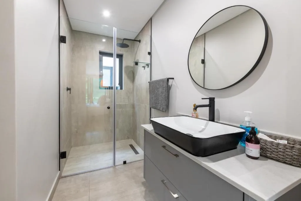 Modern bathroom with walk-in shower, black vanity sink, and round mirror