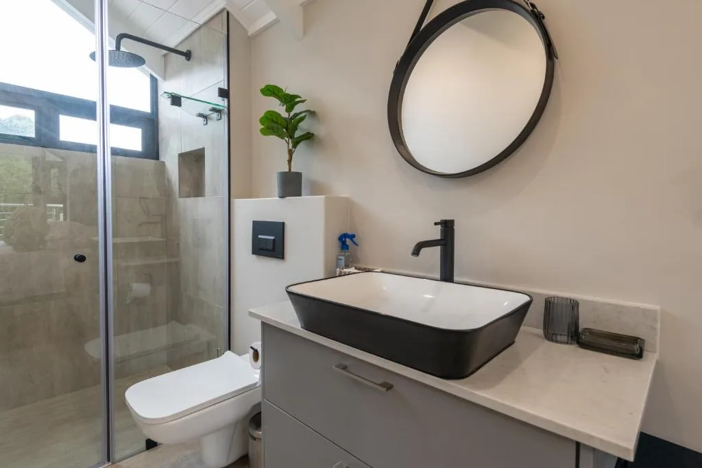 Modern bathroom with black vessel sink, round mirror, and glass shower enclosure