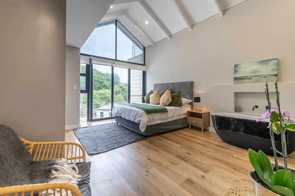 Modern bedroom with bed, large windows overlooking garden, wooden flooring, vaulted ceiling