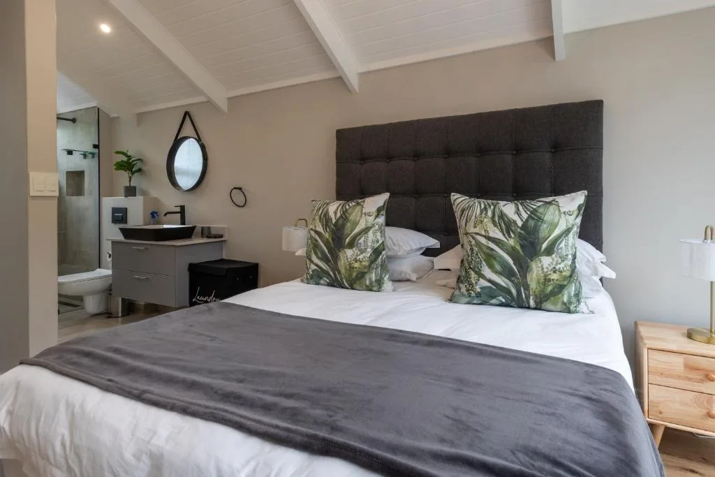 Spacious bedroom with dark headboard, tropical pillows, en-suite bathroom visible