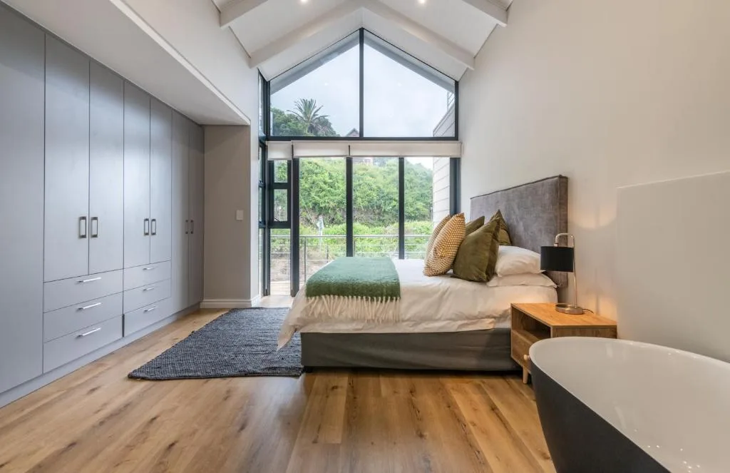 Modern bedroom with bed, green pillows, large windows overlooking garden views