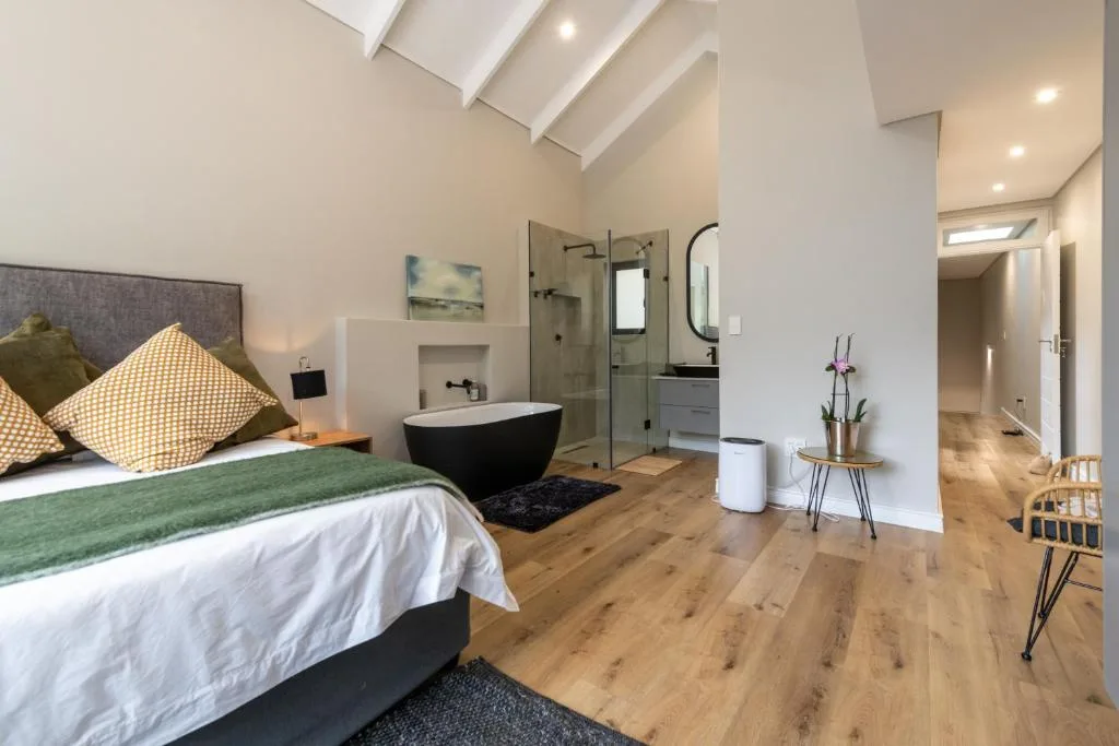 Modern bedroom with ensuite bathroom featuring freestanding black bathtub and walk-in shower