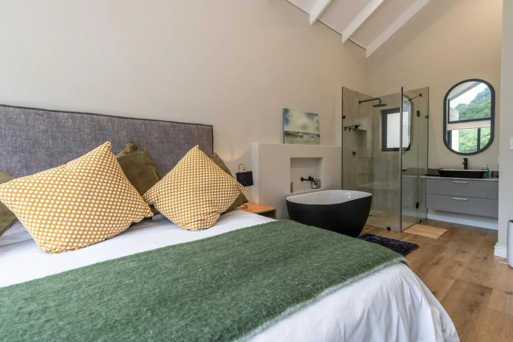 Modern bedroom with en-suite bathroom featuring freestanding black bathtub and rainfall shower