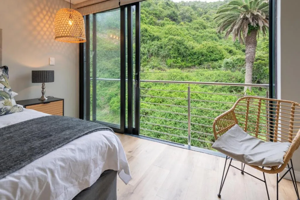 Modern bedroom with bed, woven pendant light, and expansive mountain views through glass doors