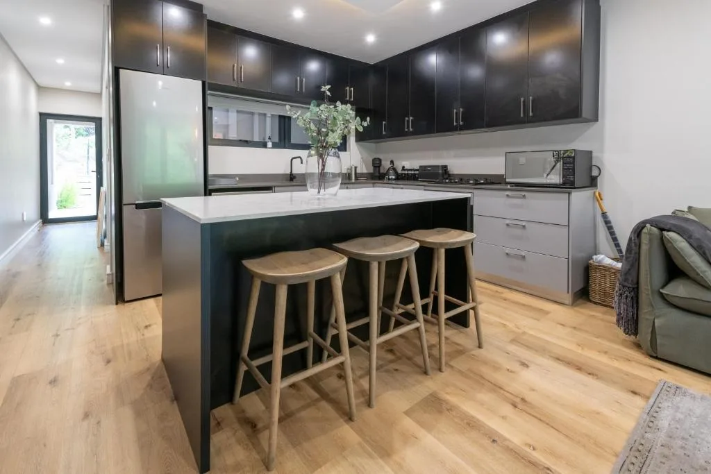 Modern black cabinetry kitchen with white countertops and wooden bar stools