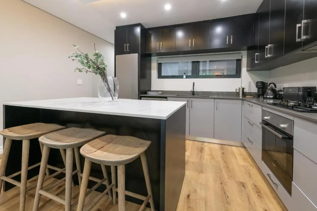 Modern kitchen with black cabinetry, white island, and wooden bar seating