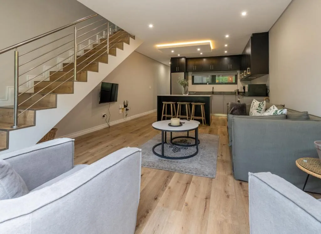Modern open-plan lounge with sofas, kitchen, and wooden staircase